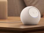 Un haut-parleur Amazon Echo Dot Max blanc sur une table en bois à côté d'une lampe.
