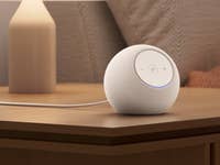 Un haut-parleur Amazon Echo Dot Max blanc sur une table en bois à côté d'une lampe.