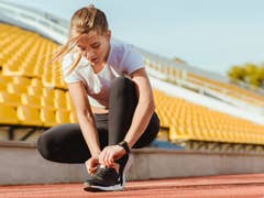 Une femme qui lace ses chaussures sur une piste de course avec des sièges de stade vides en arrière-plan.
