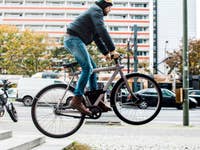 Une personne monte sur un vélo VanMoof Electrified S, effectuant un saut sur des marches en ville.