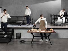 Un homme utilisant un aspirateur pendant que d'autres travaillent dans la maison.