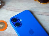 Un smartphone bleu à côté d'un AirTag Apple orange et d'écouteurs jaunes sur une surface en bois.