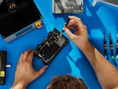 Une personne répare un appareil Apple avec des outils sur une surface de travail bleue.