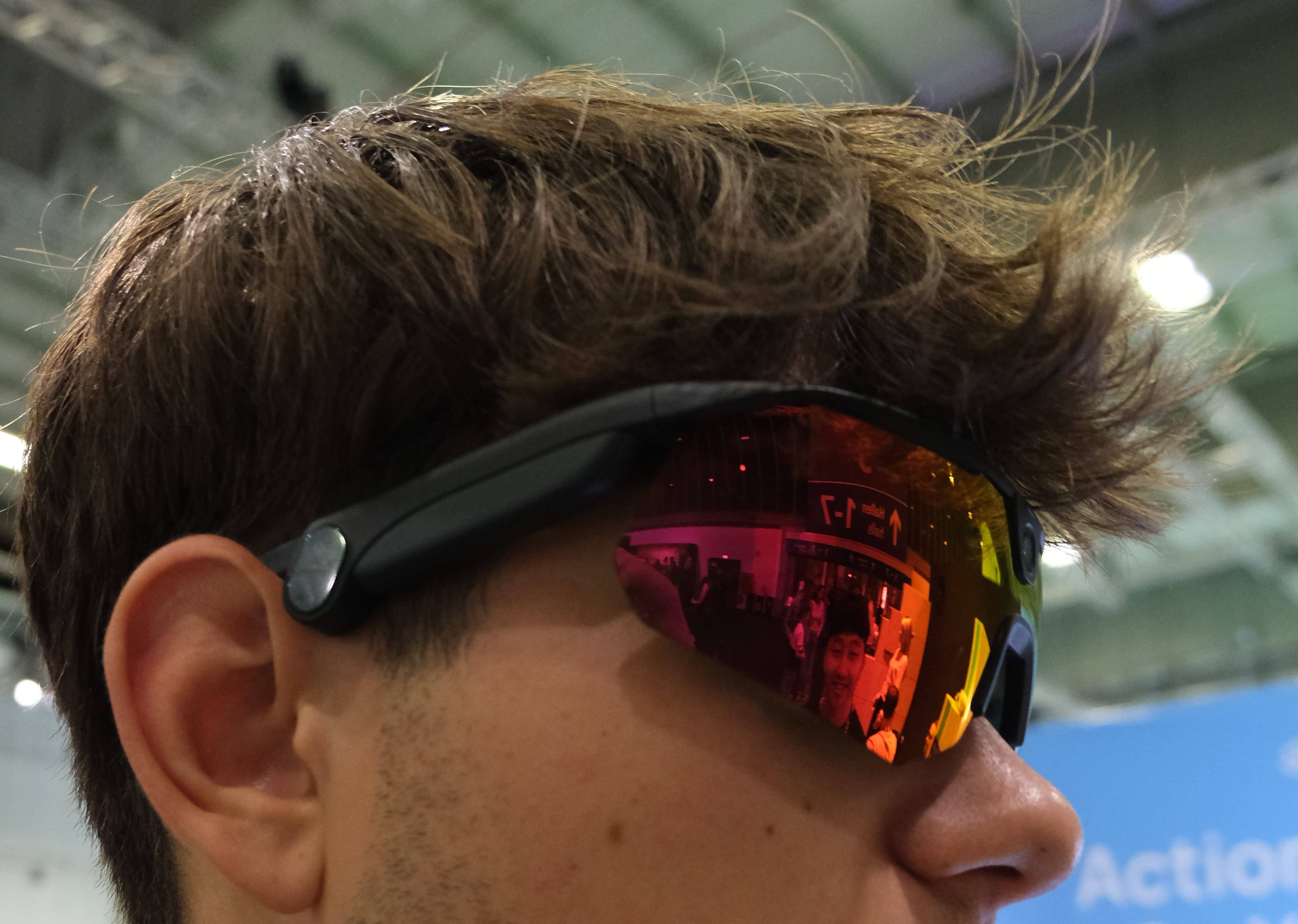 Gros plan sur une personne portant des lunettes de soleil à verres réfléchissants, montrant un arrière-plan coloré.