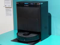 Aspirateur robot Bosch Spotless et station d'accueil exposés sur une surface turquoise.