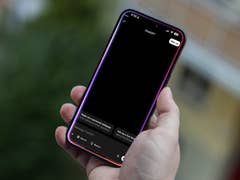 Une personne tenant un Apple iPhone 15 Pro Max avec un écran noir affichant une interface de chat.