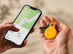 Une main tenant un smartphone affichant une carte avec un tracker Chipolo Loop et des clés.