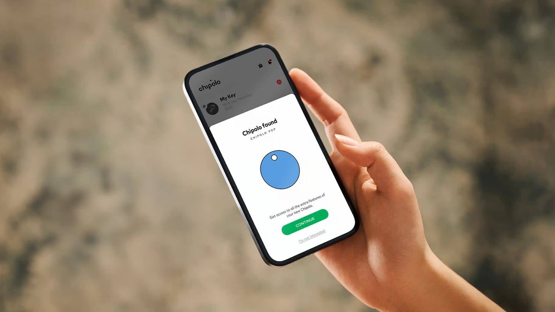 Une main tenant un smartphone affichant l'application Chipolo avec une notification Chipolo trouvé en bleu.