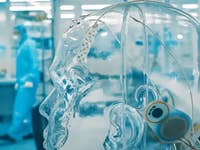 Un modèle de tête humaine transparente avec des fils et des capteurs dans un laboratoire, avec une personne en tenue de protection en arrière-plan.