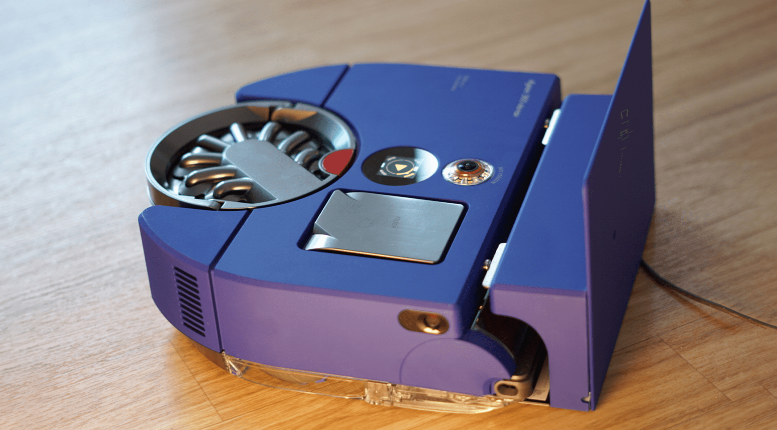 Aspirateur robot Dyson 360 Vis Nav en bleu avec un design épuré, posé sur une surface en bois. Aspirateur robot Dyson 360 Vis Nav en bleu avec un design épuré, posé sur une surface en bois.