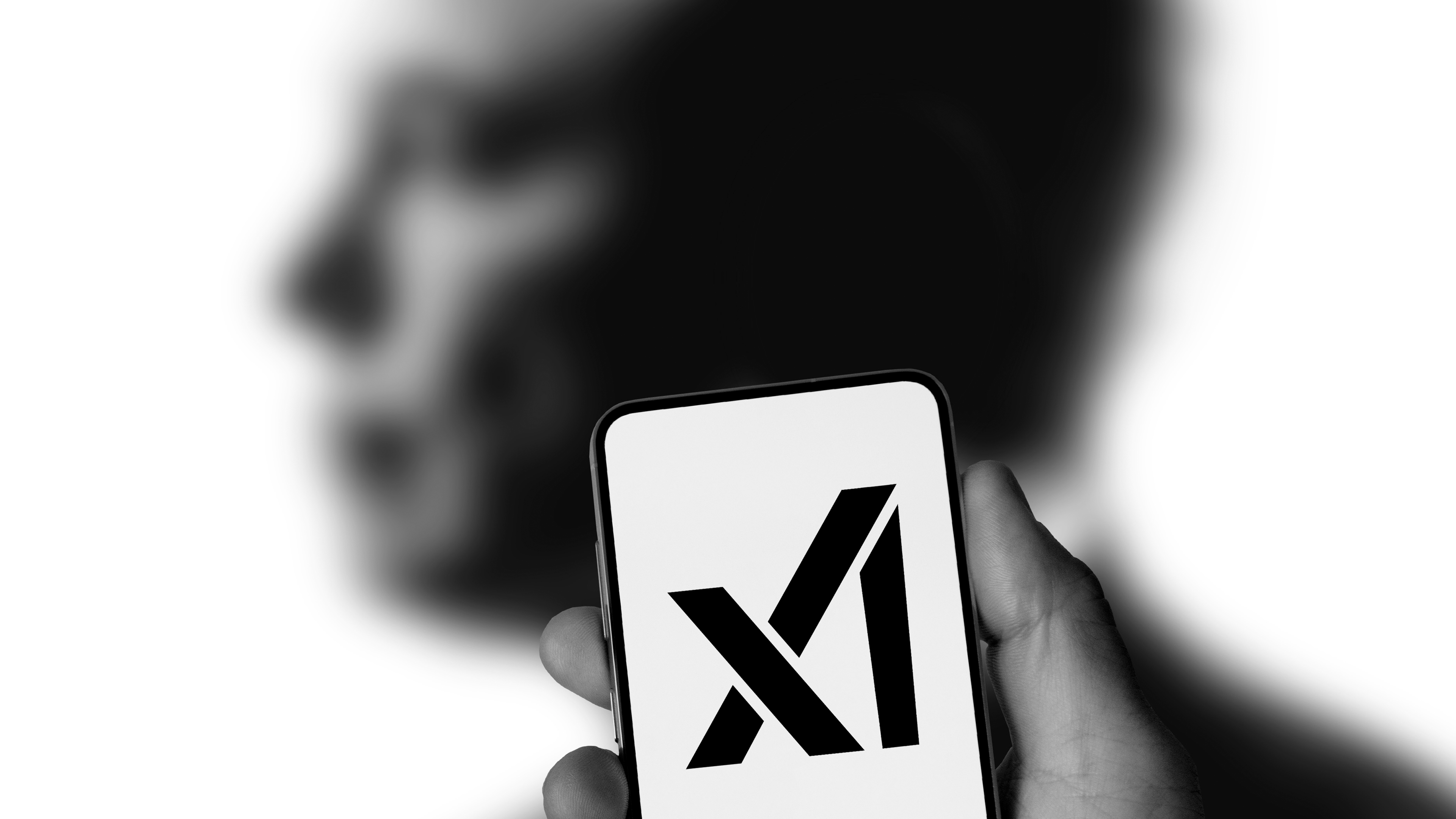 Une main tenant un smartphone affichant le logo 'X' devant une silhouette humaine floue.