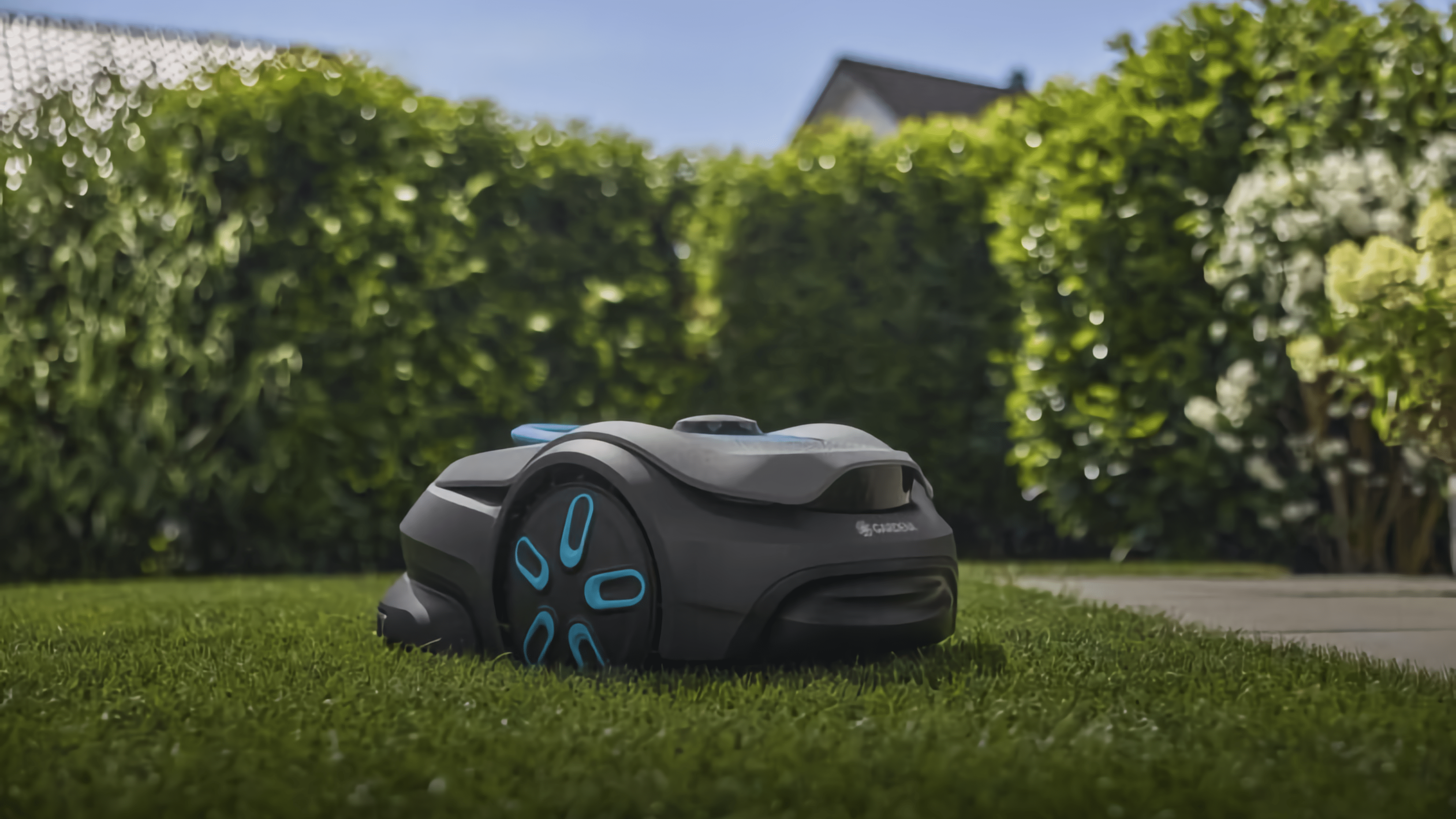 Un tondeuse robot Gardena Smart Sileno Sense sur de l'herbe verte près des haies.