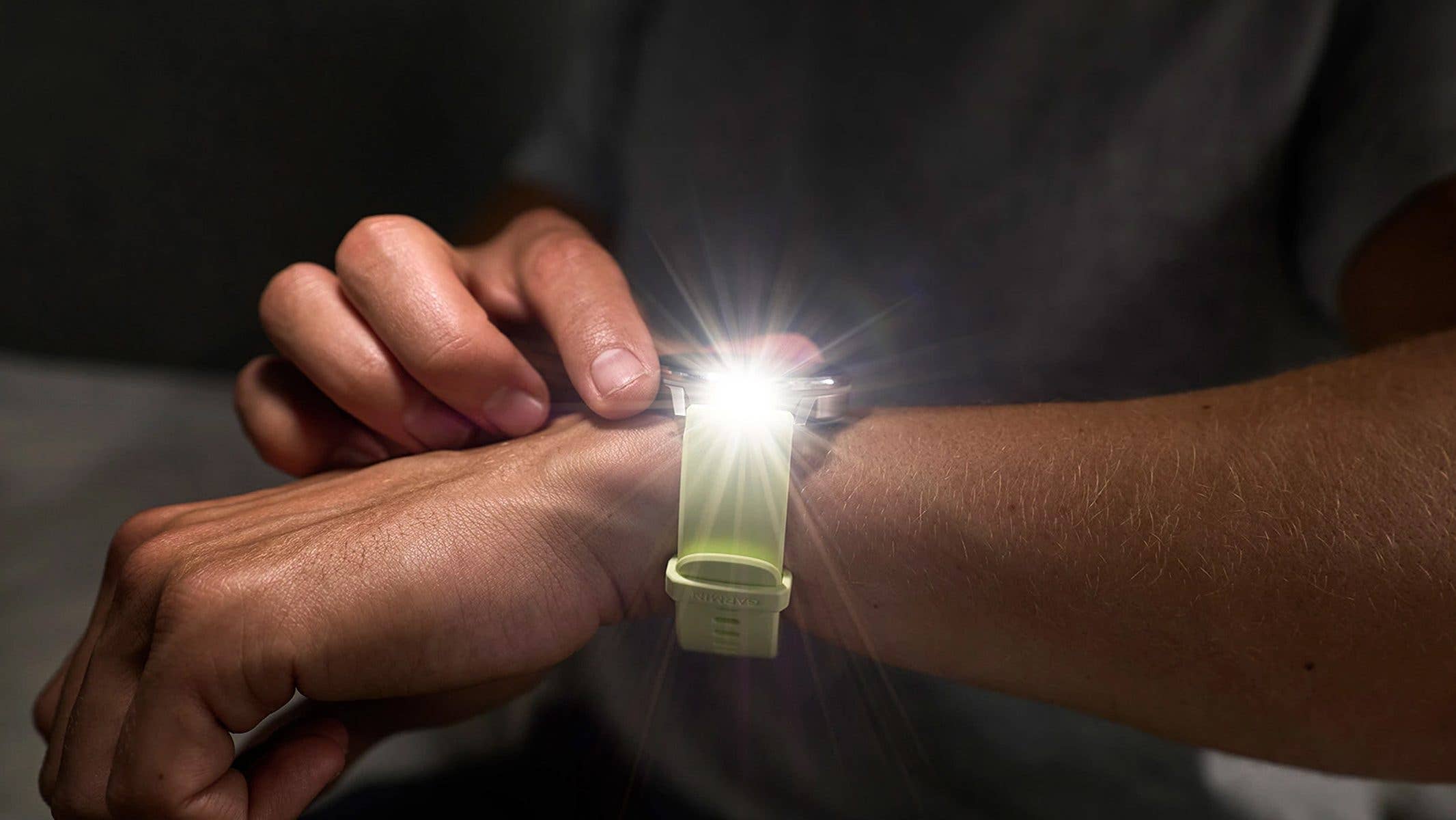 Une personne ajuste une montre Garmin Venu 4 à son poignet, avec une lumière brillante émanant de l'appareil.
