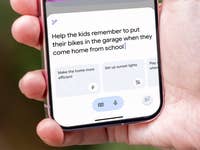 Une main tenant un smartphone affichant un rappel : 'Aidez les enfants à se souvenir de mettre leurs vélos dans le garage.'