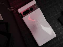 Un smartphone Google Pixel 7 Pro avec un dos fissuré, reposant sur une surface noire texturée avec des trombones et des fournitures de bureau.