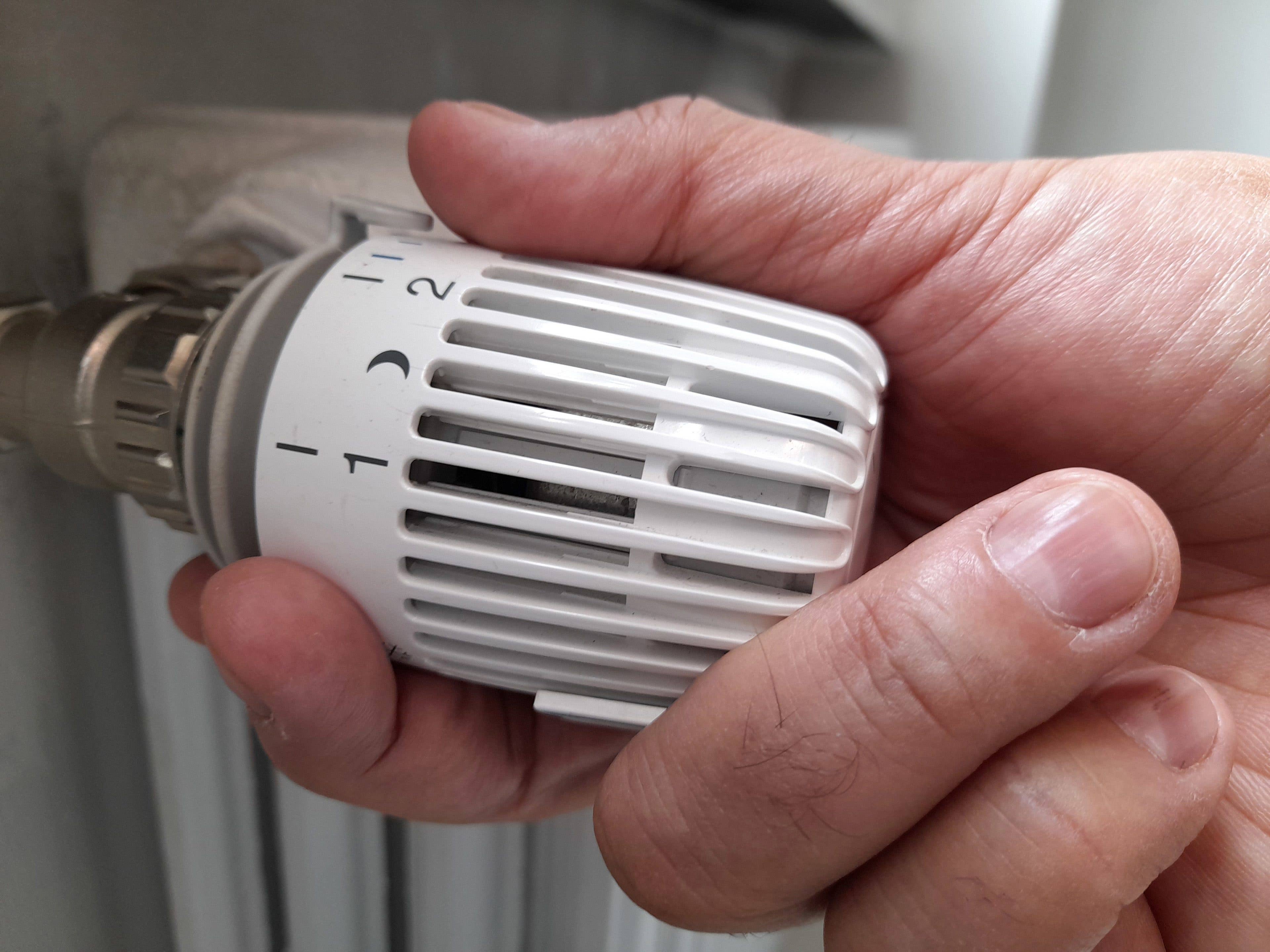 Une main réglant une vanne de thermostat sur un radiateur.