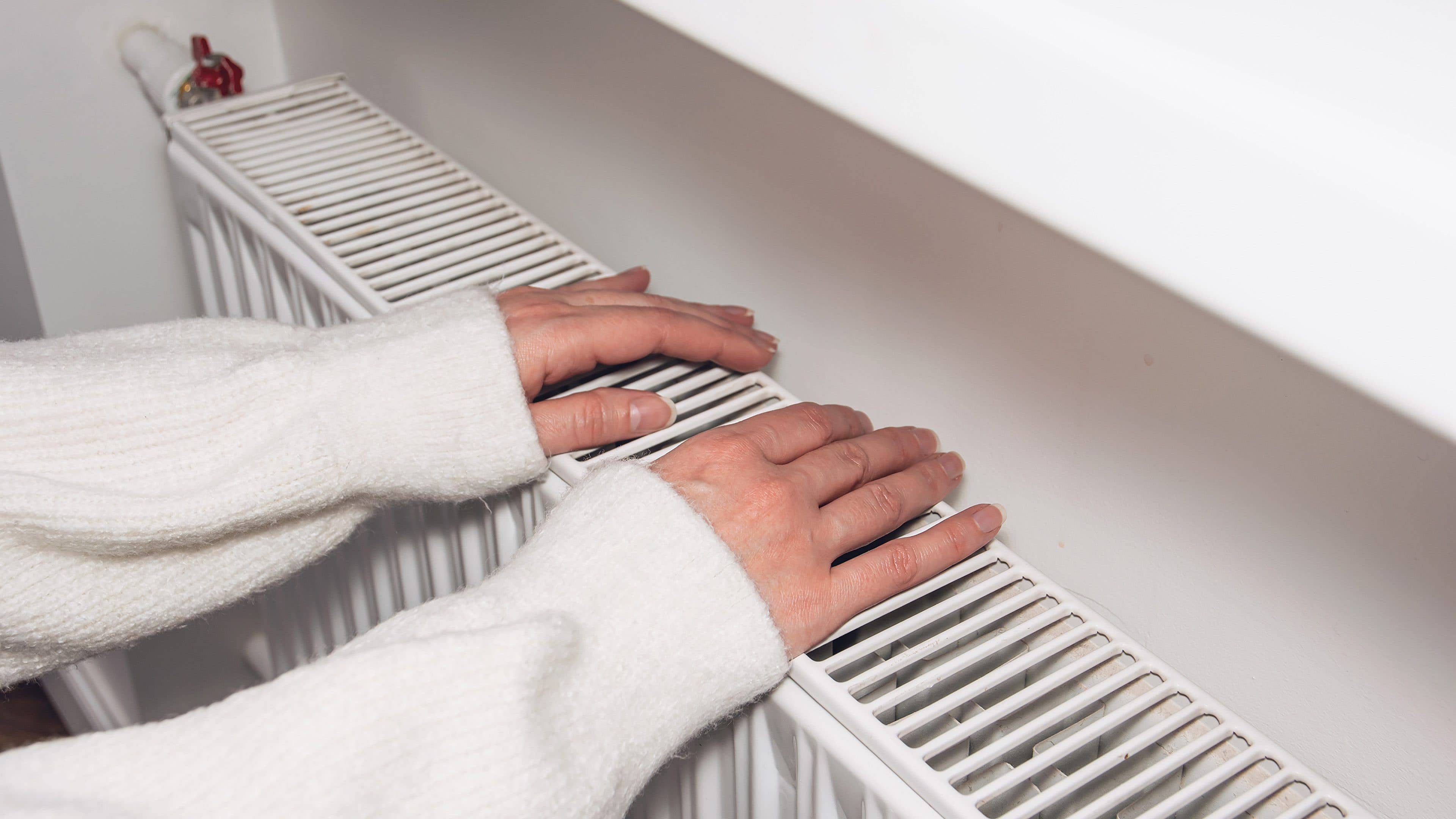 Des mains reposent sur un radiateur blanc.