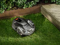 Une tondeuse robot Husqvarna sur de l'herbe verte près d'une terrasse en bois.
