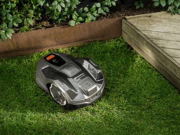 Une tondeuse robot Husqvarna sur de l'herbe verte près d'une terrasse en bois.