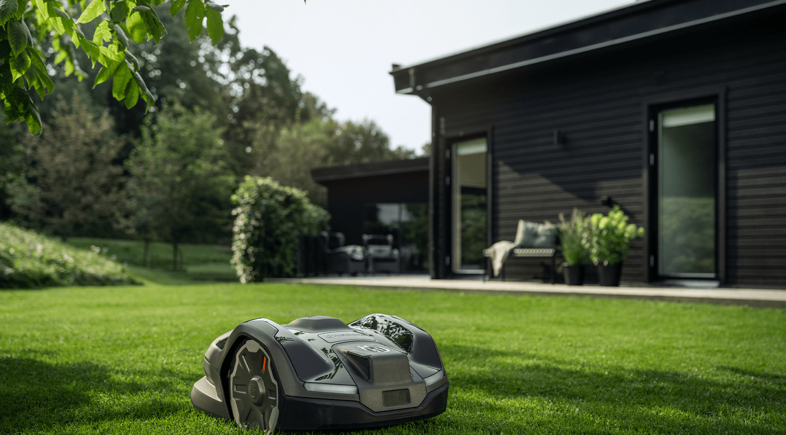Une tondeuse à gazon robot Husqvarna 405XE Nera sur une pelouse bien entretenue près d'une maison moderne noire.