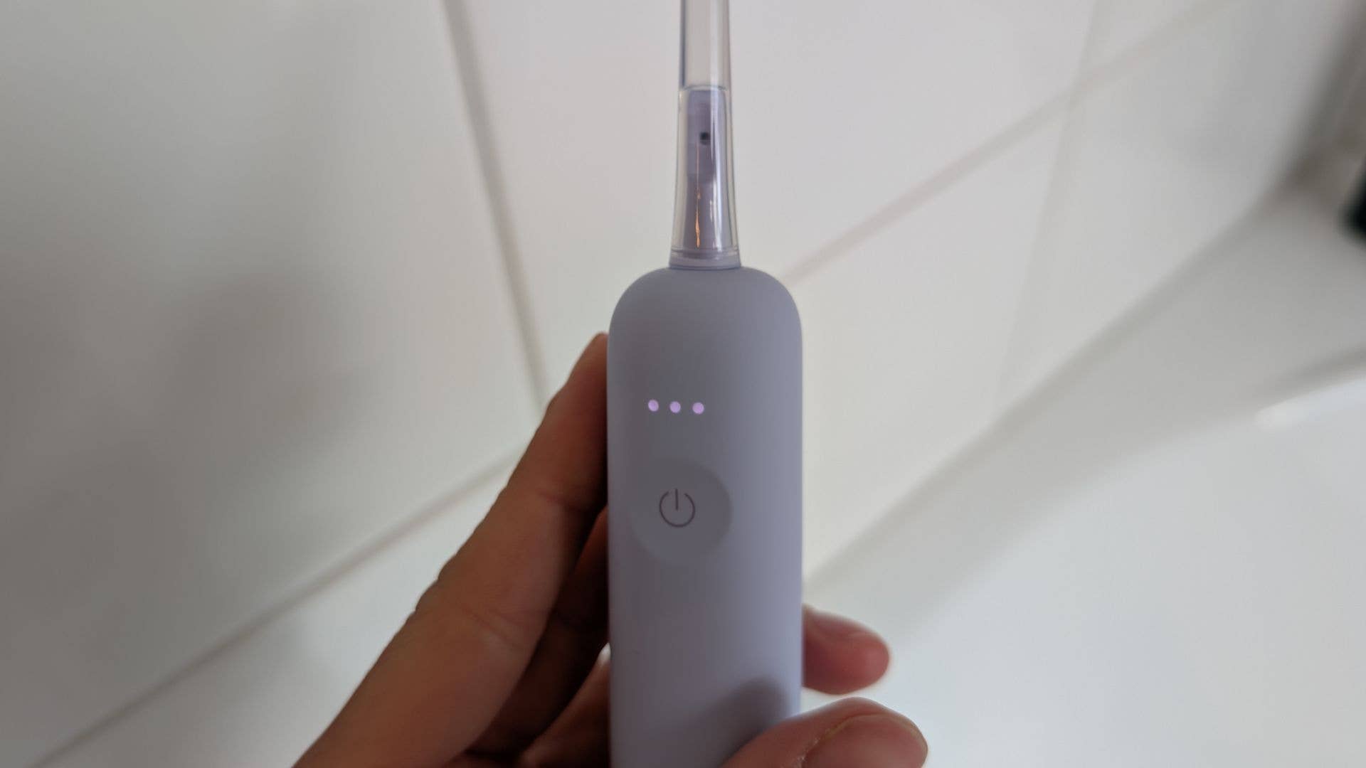 Une main tenant une brosse à dents électrique grise avec une tête transparente et trois voyants lumineux.