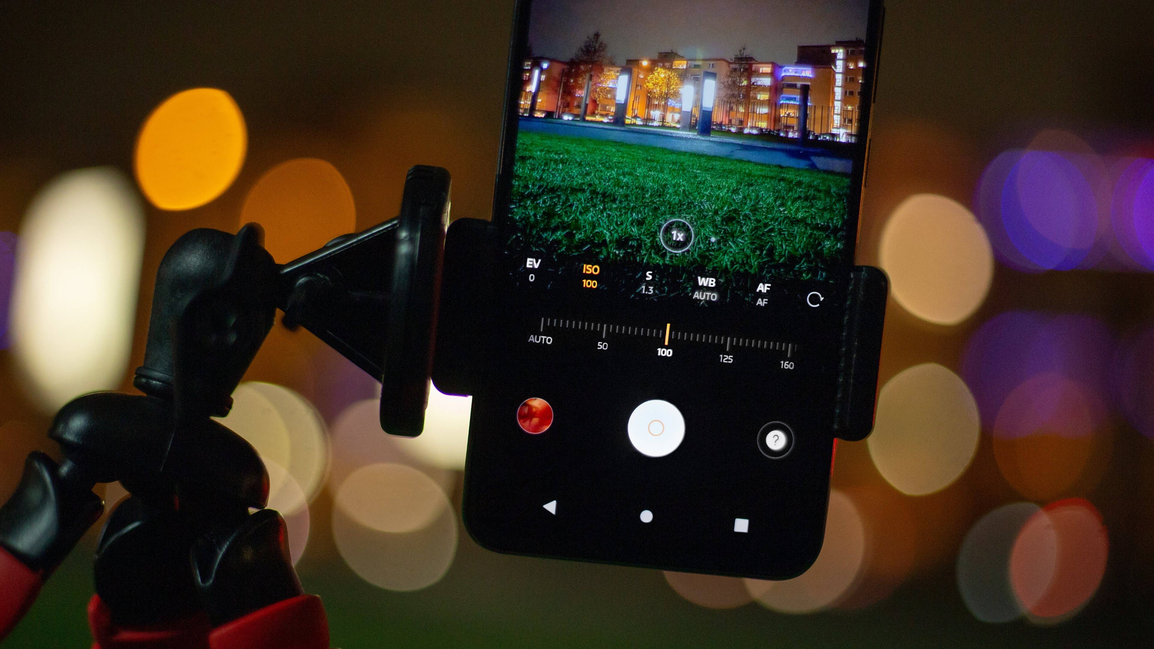 Un smartphone montado en un trípode que muestra configuraciones de fotografía nocturna con luces coloridas borrosas de fondo.