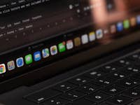 Gros plan d'un écran d'ordinateur portable montrant l'icône Google Chrome dans le dock avec du texte de codage en arrière-plan.