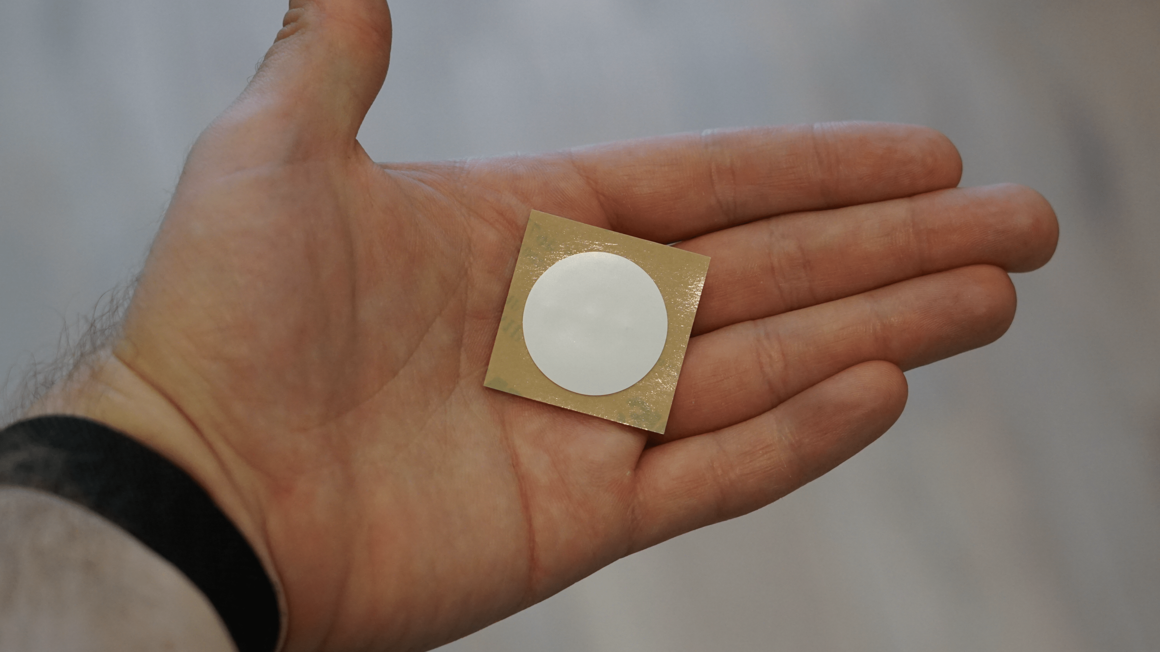 Une main tenant un autocollant NFC circulaire sur un fond doré.