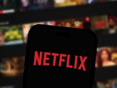 Un smartphone affichant le logo de Netflix sur un fond flou de vignettes de films.