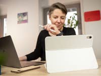 Une femme utilisant un Apple iPad 2022 blanc avec un stylet assise à un bureau avec un ordinateur portable.