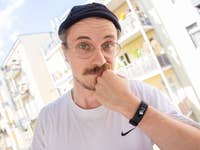Une personne avec des lunettes et une moustache se tient le menton, portant une montre Garmin Vivosmart 5.