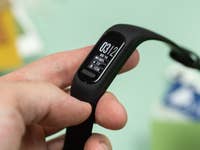 Une personne tient un bracelet de fitness Garmin Vivosmart 5 affichant l'heure et les statistiques d'activité.