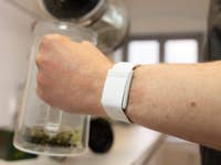 Une main tenant une théière en verre avec une montre intelligente blanche au poignet.