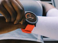 Gros plan sur une montre connectée noire et orange au poignet, une personne l'ajustant.