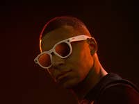 Une personne portant des lunettes de soleil blanches sur un fond sombre.