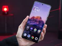 Une main tient un smartphone OnePlus 13 affichant l'heure 15:41 et un fond d'écran flou.