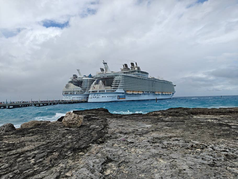 Un grand bateau de croisière amarré près des côtes rocheuses sous un ciel nuageux.