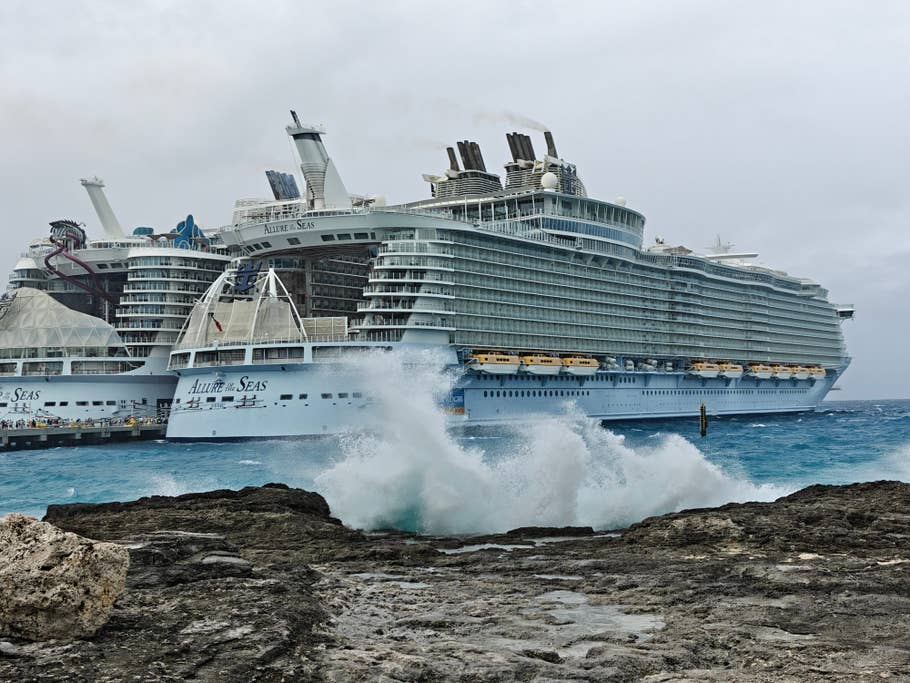 Un grand navire de croisière, Allure of the Seas, amarré près du0027une côte rocheuse avec des vagues su0027écrasant au premier plan.