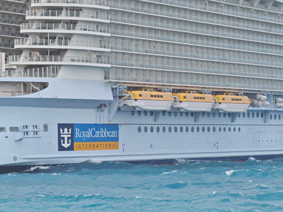 Un grand navire de croisière avec des canots de sauvetage, arborant le logo de Royal Caribbean, amarré dans des eaux turquoises.