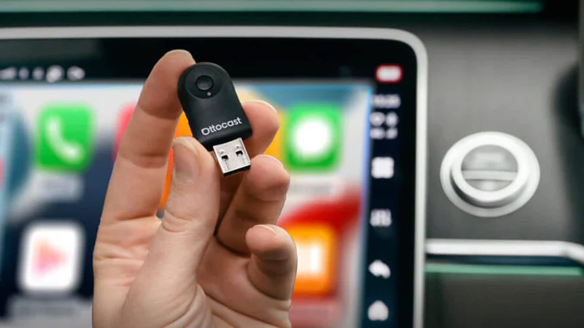 Une main tenant un appareil USB Ottocast devant un écran de tableau de bord de voiture.