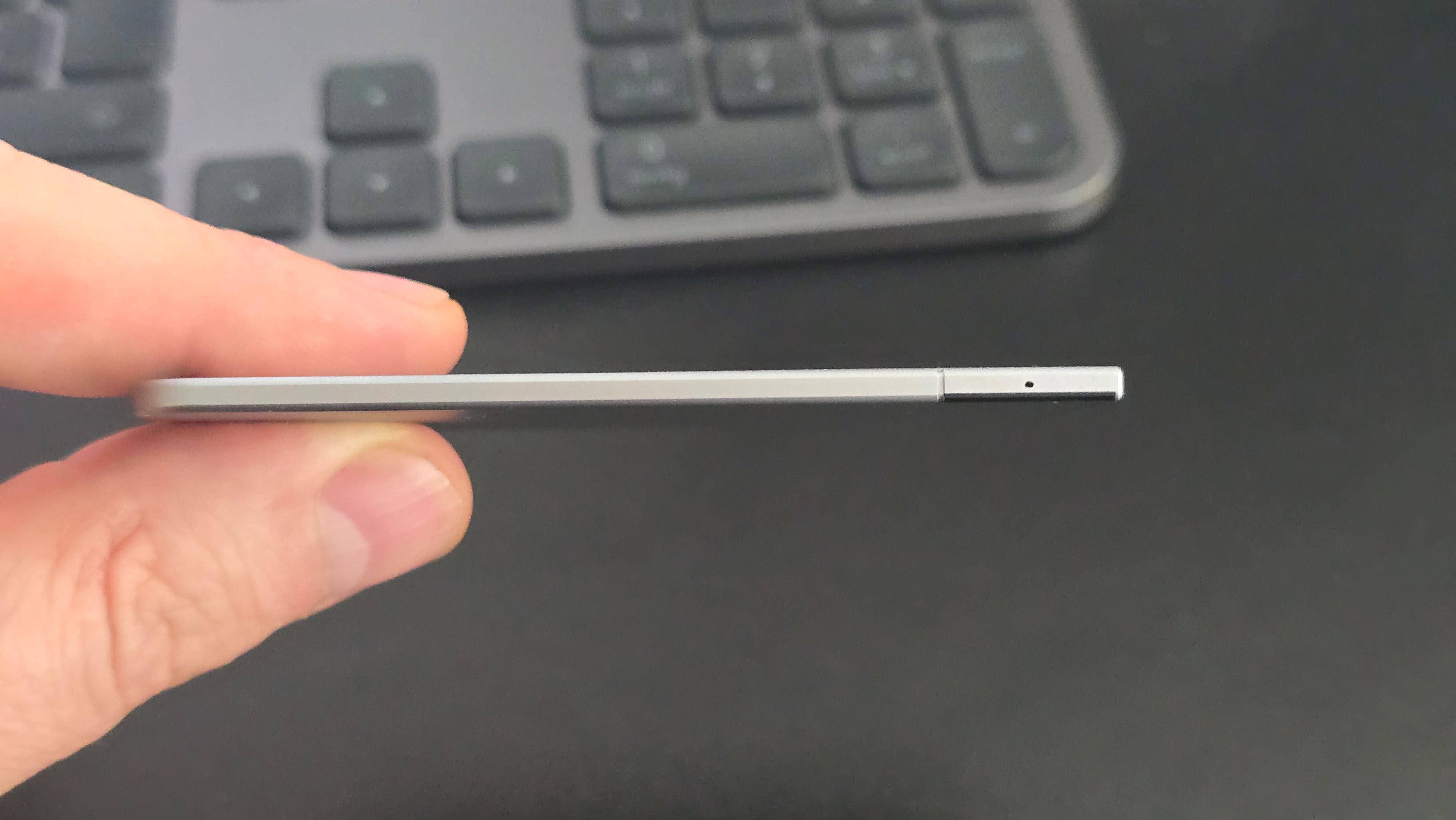 Une personne tenant un appareil mince et argenté avec un petit trou à une extrémité, en arrière-plan un clavier.