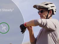 Un cycliste portant un casque consulte une montre intelligente, avec le texte 'Hold Steady' et une icône de satellite.