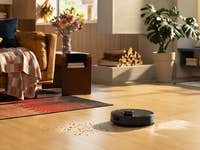 Un aspirateur robot Roborock Q10 S5+ nettoyant des débris sur un sol en bois dans un salon confortable.