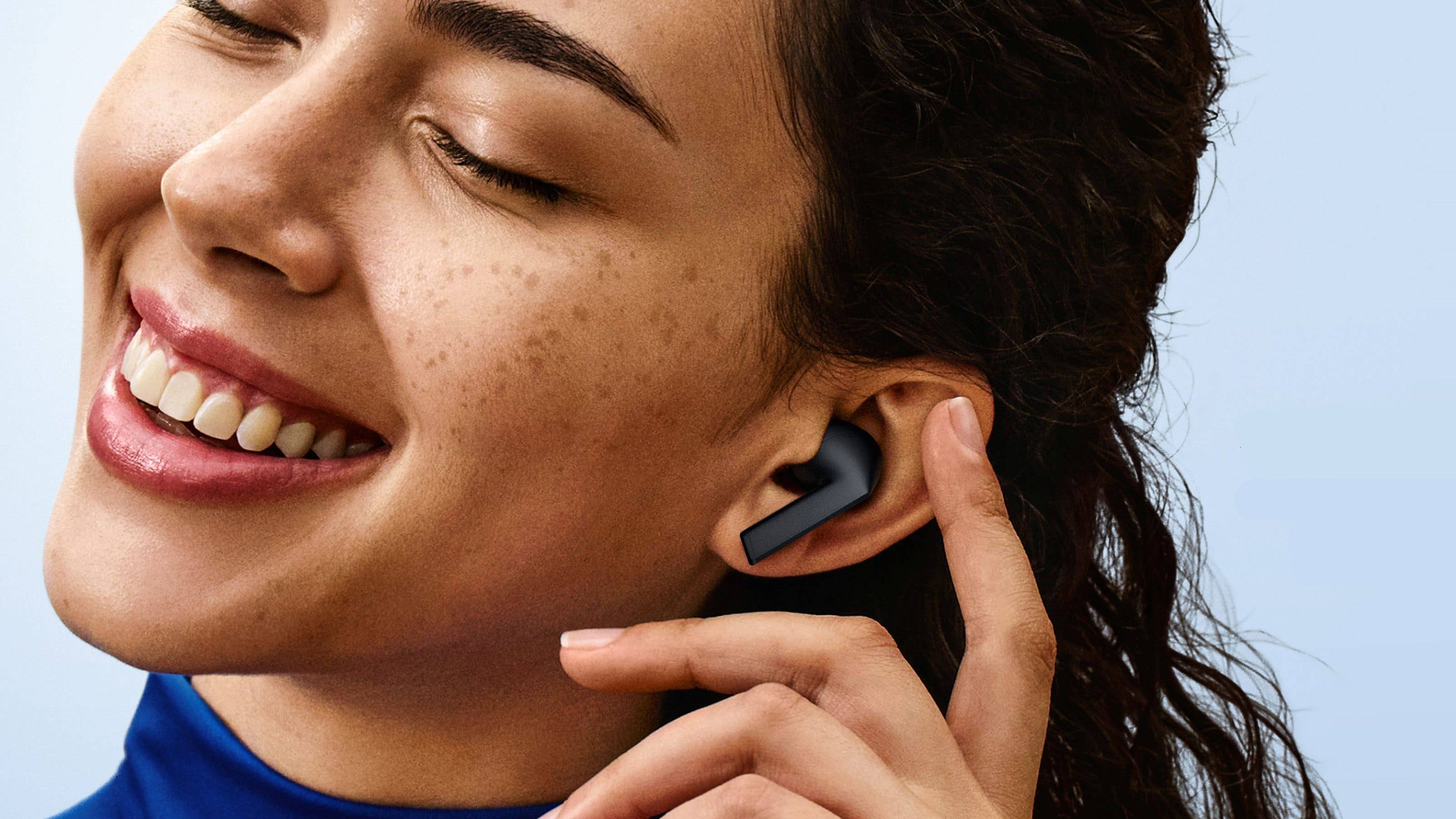 Une personne souriante ajustant les Samsung Galaxy Buds 3 FE dans son oreille.