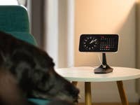 Un iPhone posé sur une table, présentant la fonction Smart Display d'iOS 17, tandis qu'un chien se prélasse sur le canapé.