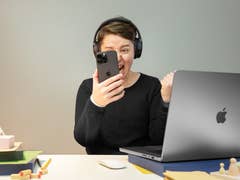 Personne avec des écouteurs tenant un smartphone avec excitation devant un ordinateur portable.