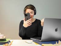 Personne avec des écouteurs tenant un smartphone avec excitation devant un ordinateur portable.