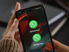 Une main tenant un smartphone affichant l'icône de l'application WhatsApp deux fois à l'écran.