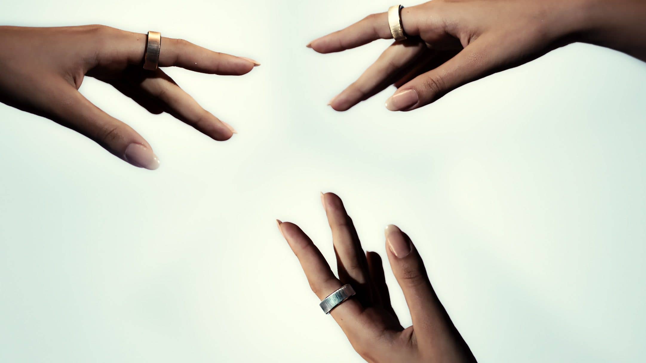 Deux mains se tendant l'une vers l'autre, présentant des bagues sur les doigts sur un fond clair.