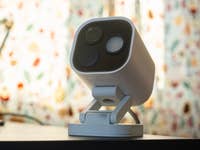 Un hub de caméra Aqara G5 Pro blanc sur une surface noire avec un fond à motifs colorés.